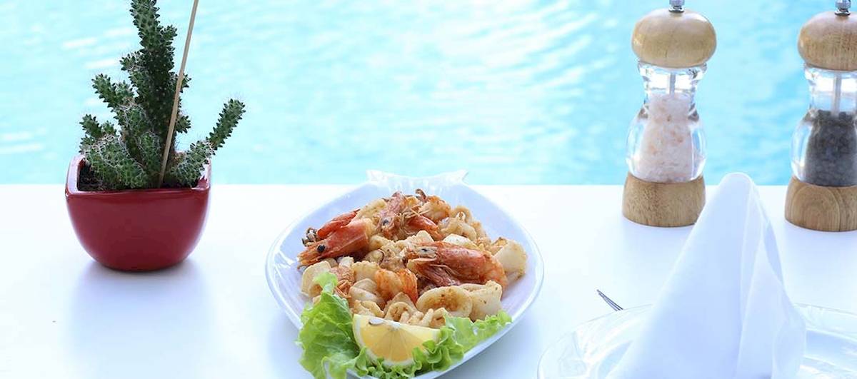 Nahaufnahme eines gegrillten Garnelen- und Tintenfischtellers mit Salat und Zitrone auf einem Tisch neben dem Dyrrah Hotel Pool