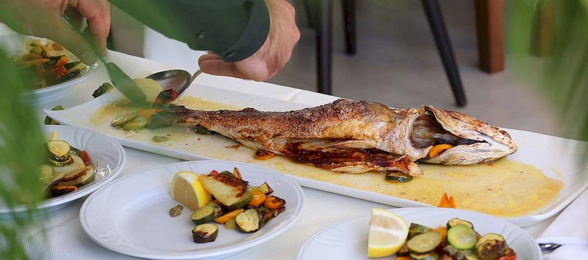 Eine Person serviert frischen Fisch auf einem Teller im Dyrrah Hotel.