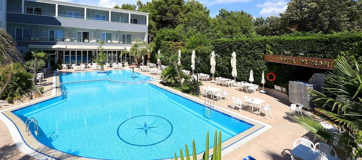 Außenbereich des Dyrrah Hotels mit Swimmingpool, weißen Tischen und Stühlen, umgeben von Pflanzen.