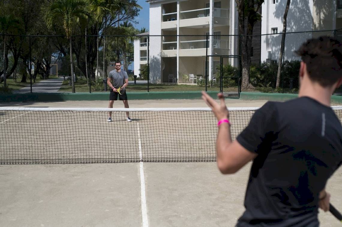 Zwei Männer spielen Tennis auf einem Platz vor einem Hotel.