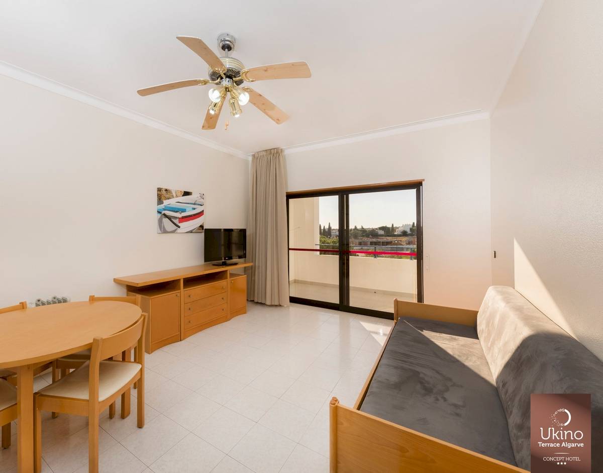 Inneneinrichtung eines Zimmers im Ukino Terrace Algarve Hotel mit Tisch, Stühlen, Fernseher und Balkon