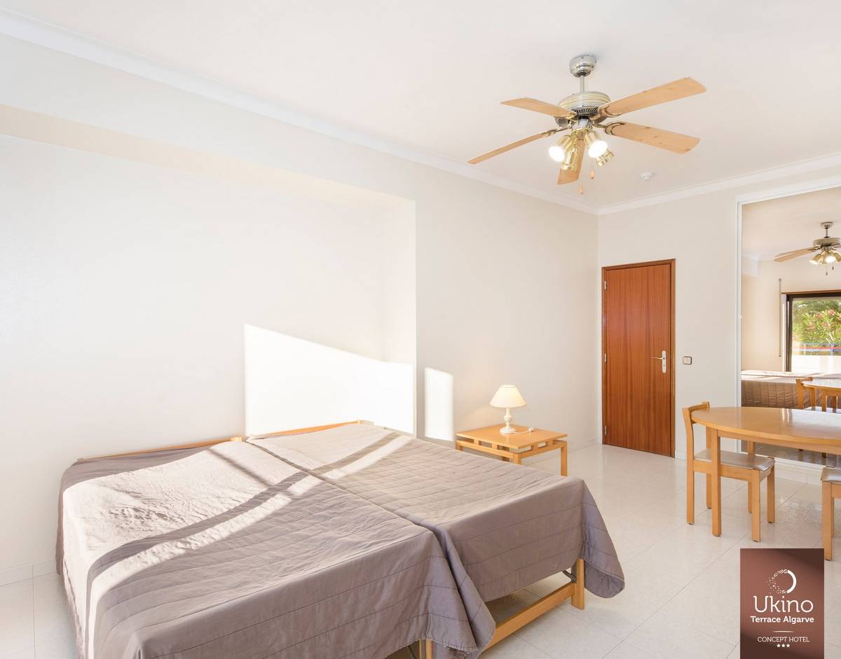 Innenansicht eines Schlafzimmers im Ukino Terrace Algarve Hotel mit zwei Betten, Nachttisch, Lampe, Esstisch und Stühlen.