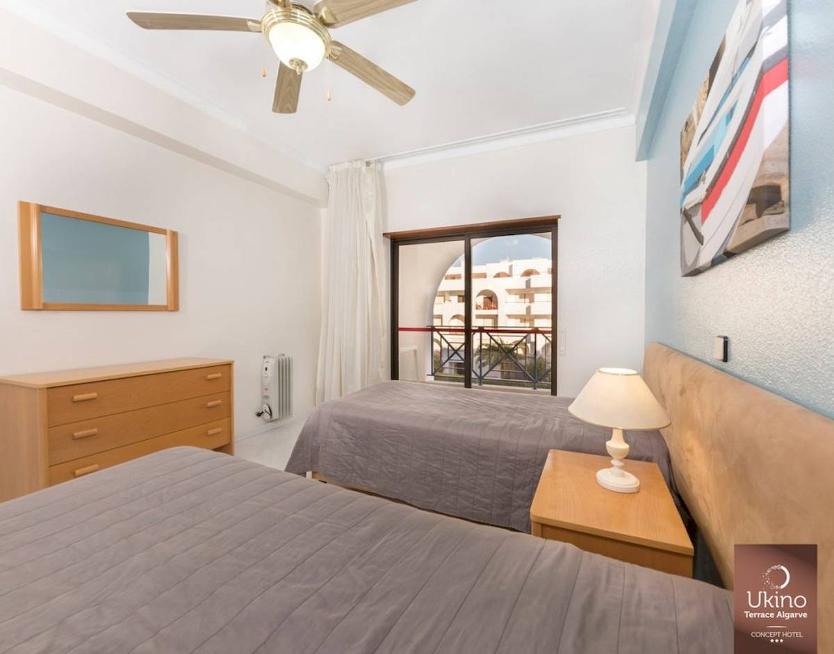 Schlafzimmer im Ukino Terrace Algarve mit zwei Betten, Nachttischen, Lampen und einem Fenster mit Balkon.