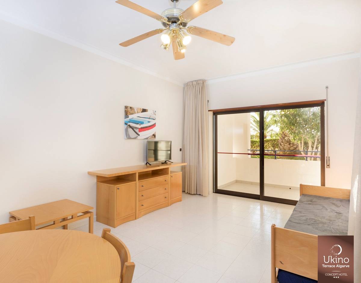 Innenraum des Ukino Terrace Algarve Hotels mit Wohnzimmer, Fernseher, Tisch und Stühlen.
