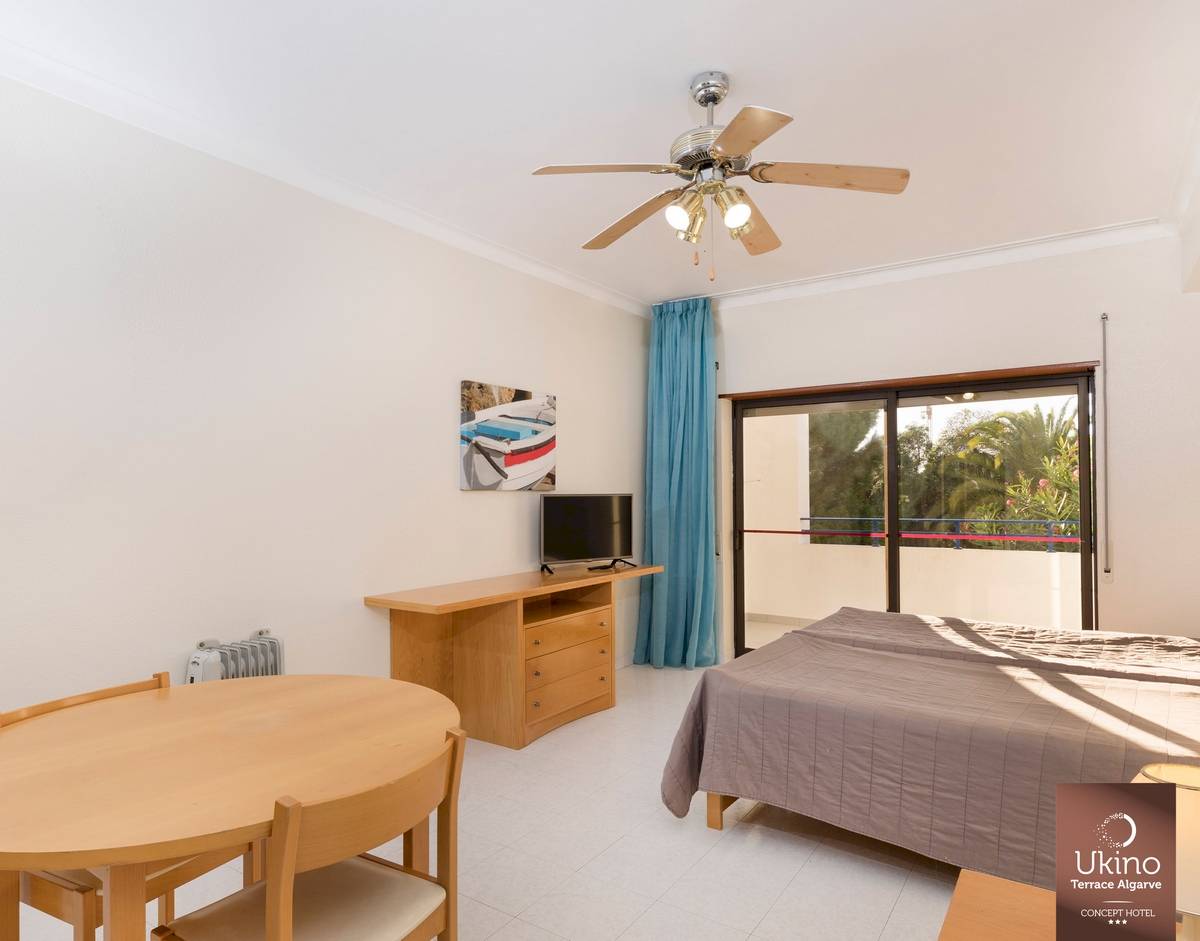 Innenansicht eines Zimmers im Ukino Terrace Algarve Hotel mit Bett, Tisch, Fernseher und Balkon.