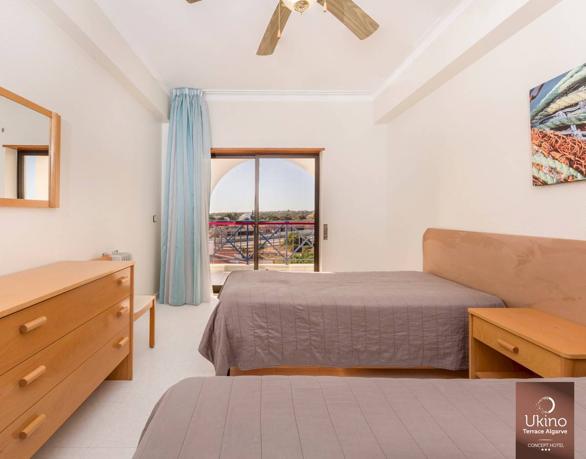 Schlafzimmer im Ukino Terrace Algarve Hotel mit zwei Betten, Kleiderschrank, Nachttisch und Balkonzugang.