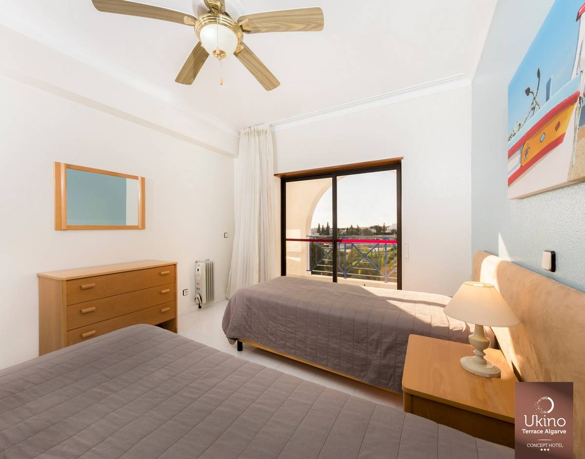 Schlafzimmer im Ukino Terrace Algarve Hotel mit zwei Betten, Nachttischen, Lampe, Spiegel und Klimaanlage.