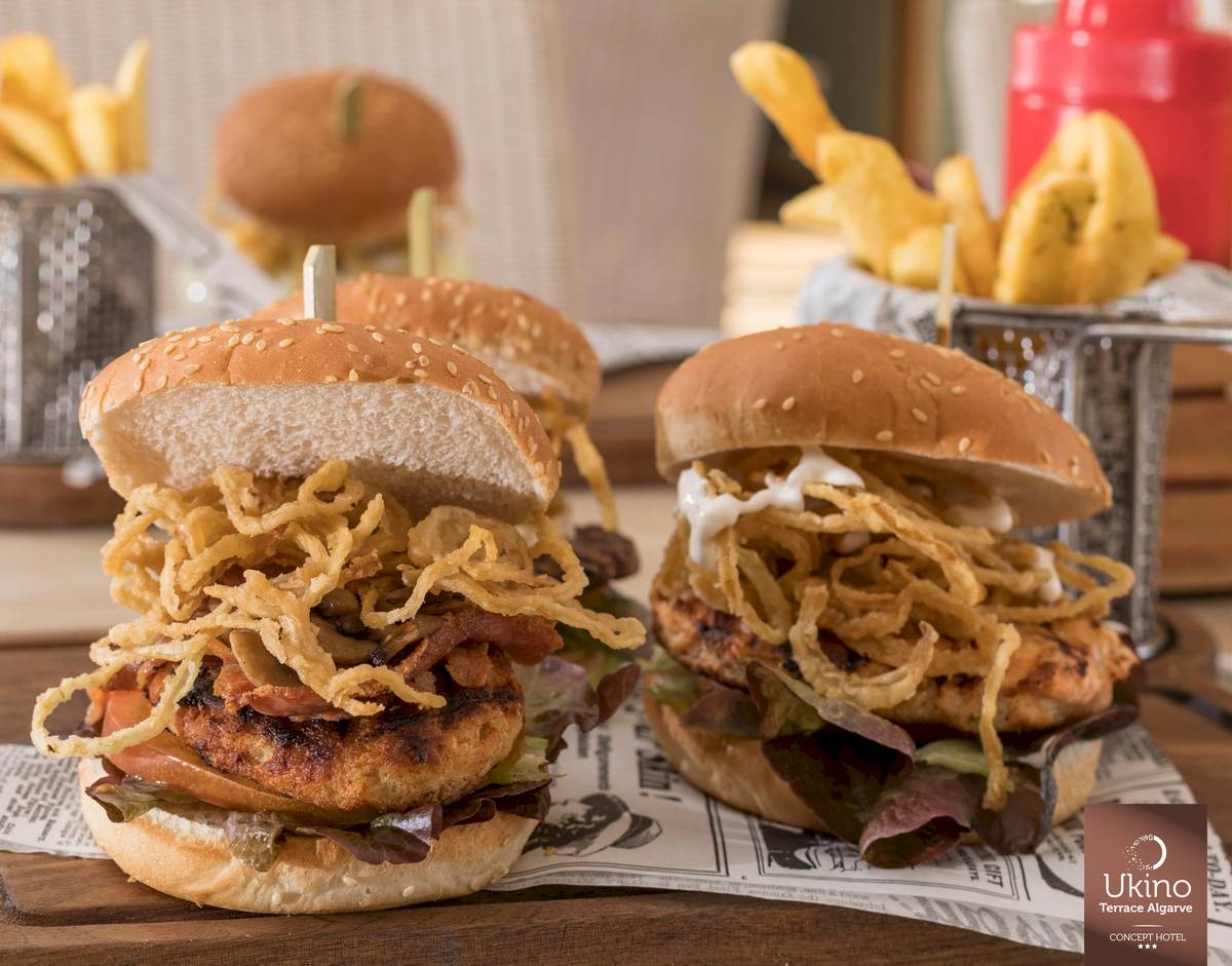 Hühnchenburger mit gebratenen Zwiebeln und Pommes frites auf einer Holzplatte.