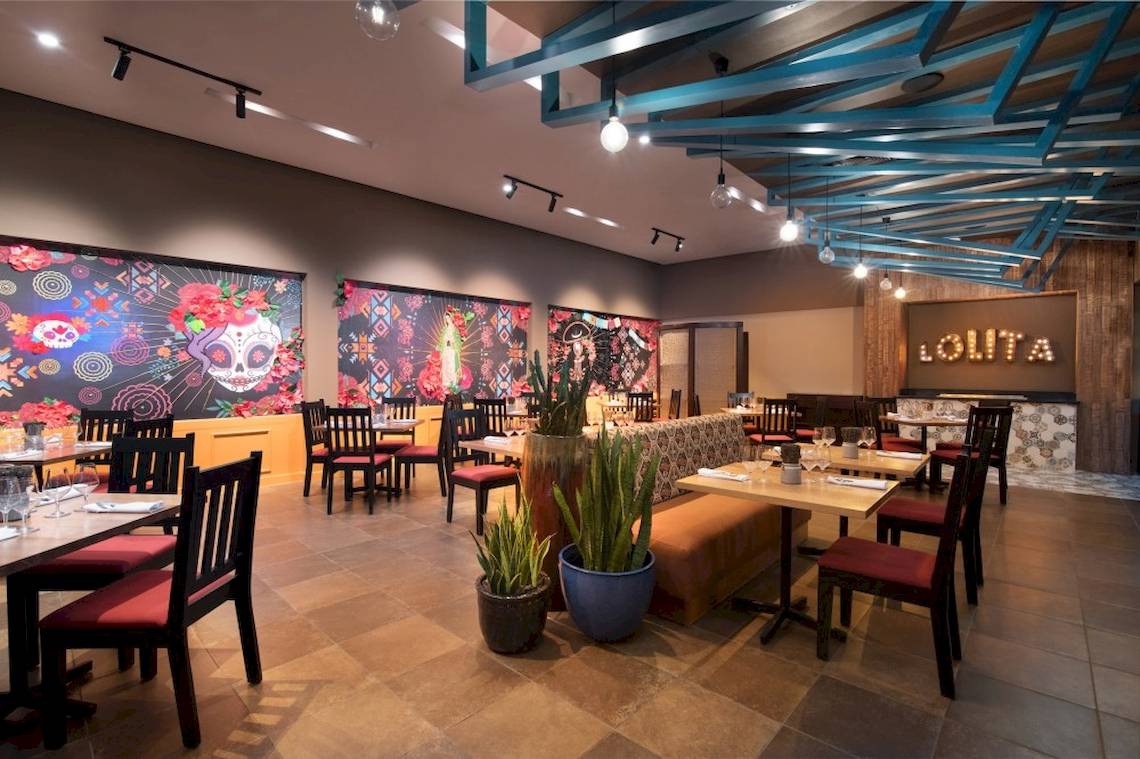 Innenansicht des Emotions By Hodelpa Puerto Plata Restaurants mit Tisch und Stühlen, Pflanzen und Wandkunst.