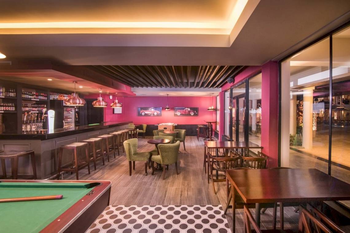 Innenbereich des Barbereichs im Emotions By Hodelpa Hotel in Puerto Plata mit grünen Stühlen und Tischen.