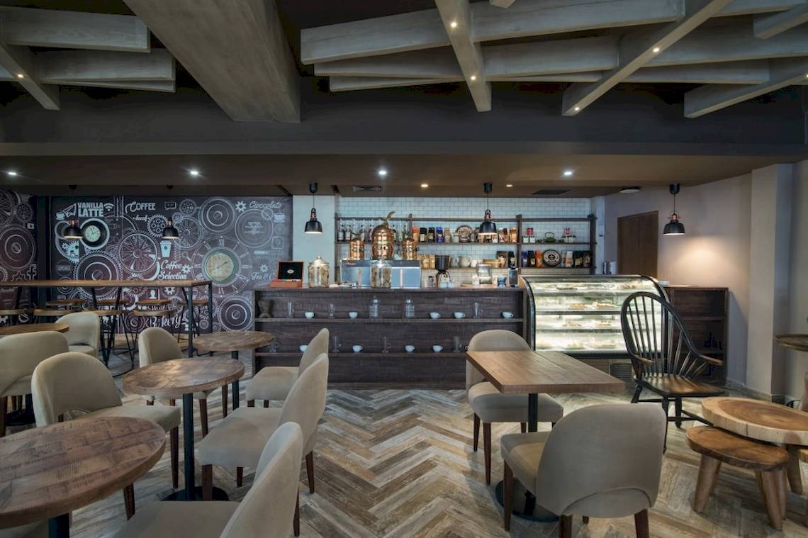 Innenansicht des Cafés im Emotions By Hodelpa Hotel in Puerto Plata mit Tischen, Stühlen und Theke.
