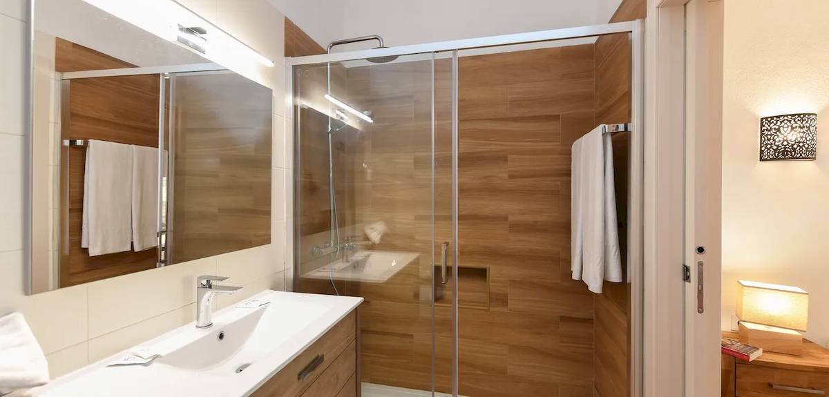 Badezimmer im Pedras da Rainha Resort mit holzvertäfelten Wänden, einer Glasdusche und einem Waschbecken.
