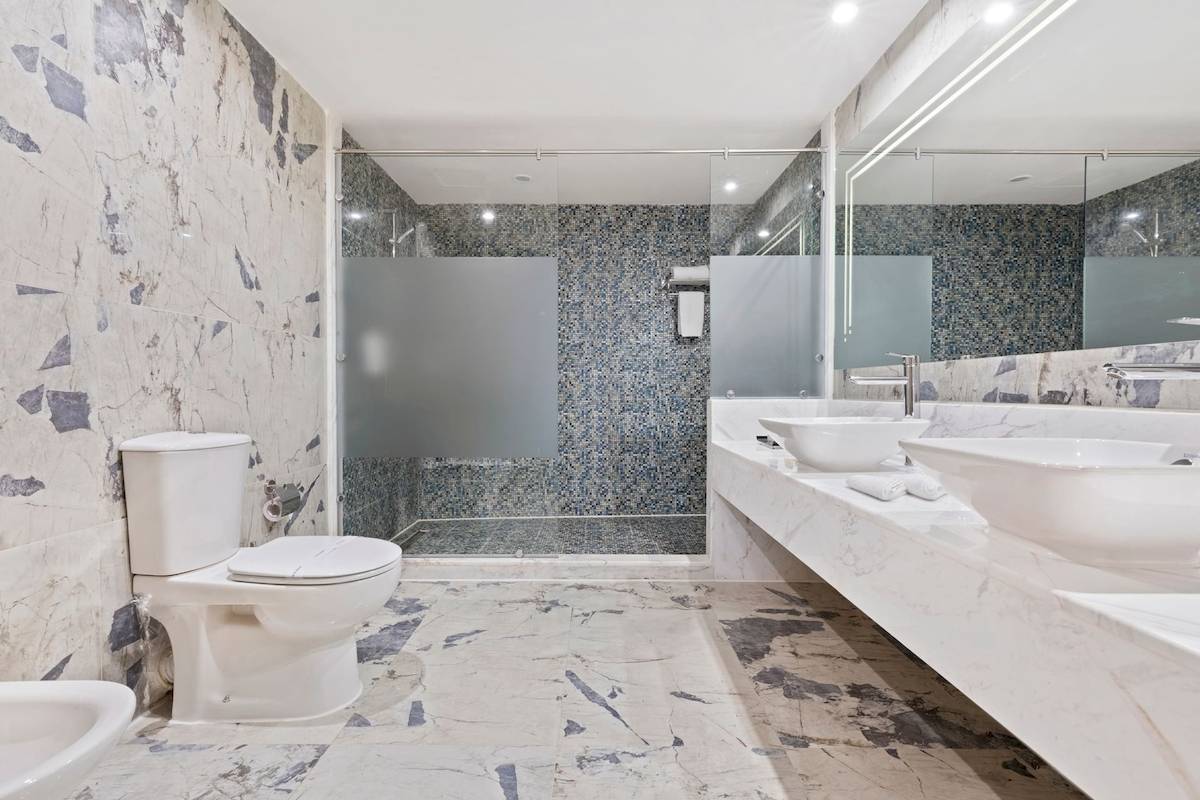 Badezimmer im Pickalbatros Blu Spa Resort mit Marmorboden, Dusche und zwei Waschbecken.