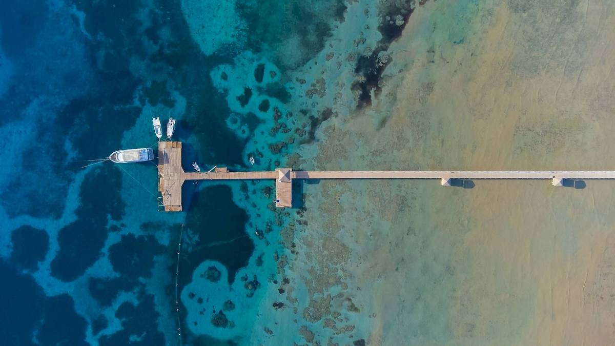Luftaufnahme des Amwaj Beach Clubs mit Pier im Wasser und mehreren Booten