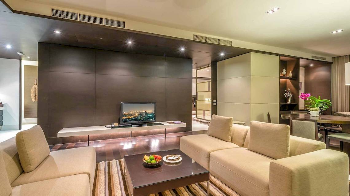 Das Wohnzimmer im Chatrium Hotel Riverside Bangkok mit modernen Möbeln und einem Fernseher.