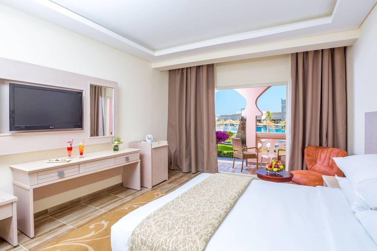 Innenansicht eines Hotelzimmers im Pickalbatros Aqua Vista Resort mit einem Bett, Fernseher, Schreibtisch und Balkon.