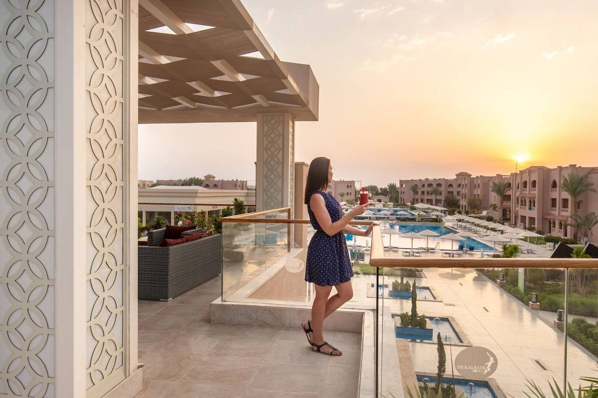Frau auf dem Balkon des Pickalbatros Aqua Vista Resorts mit Blick auf den Pool bei Sonnenuntergang.
