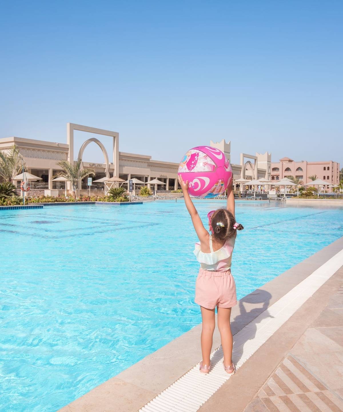 Ein junges Mädchen am Rand des Swimmingpools des Pickalbatros Aqua Vista Resorts, das einen rosa Ball hochhält