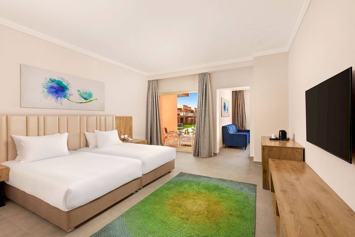 Innenansicht eines Zimmers im Pickalbatros Water Valley Resort by Neverland mit zwei Betten, Fernseher, Tisch und Sofa.