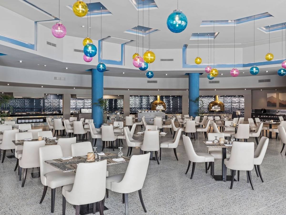 Innenansicht des Restaurants im Pickalbatros Water Valley Resort by Neverland mit vielen Tischen und Stühlen, farbigen Deckenleuchten und blauen Säulen.