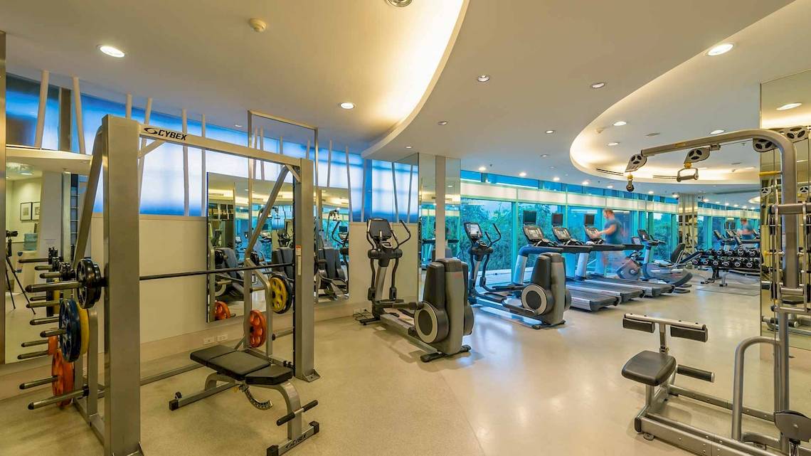 Fitnesscenter im Chatrium Hotel Riverside Bangkok mit modernen Geräten und großen Fenstern.