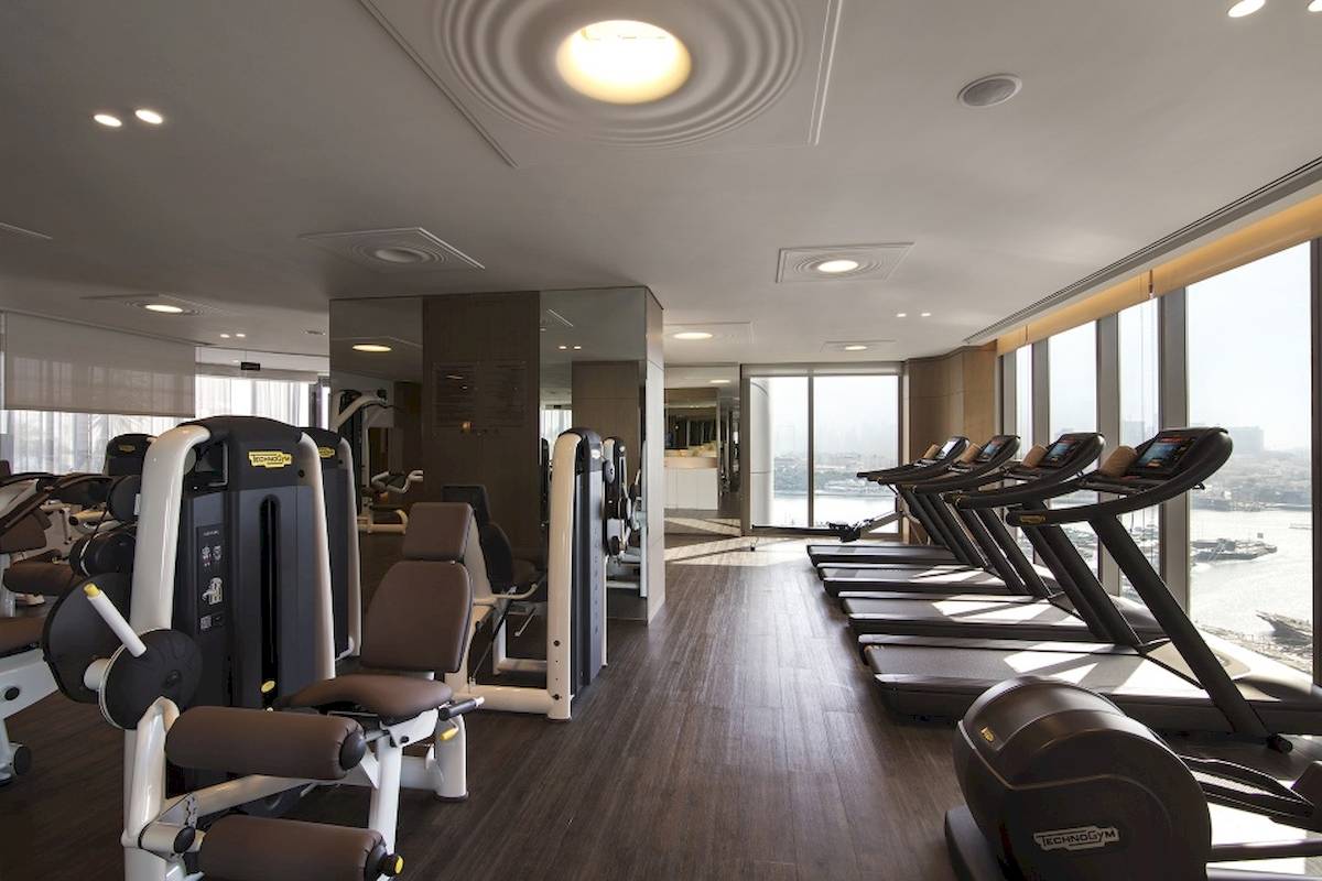 Fitnessstudio im Al Bandar Rotana Hotel mit Blick auf das Meer und modernen Geräten.