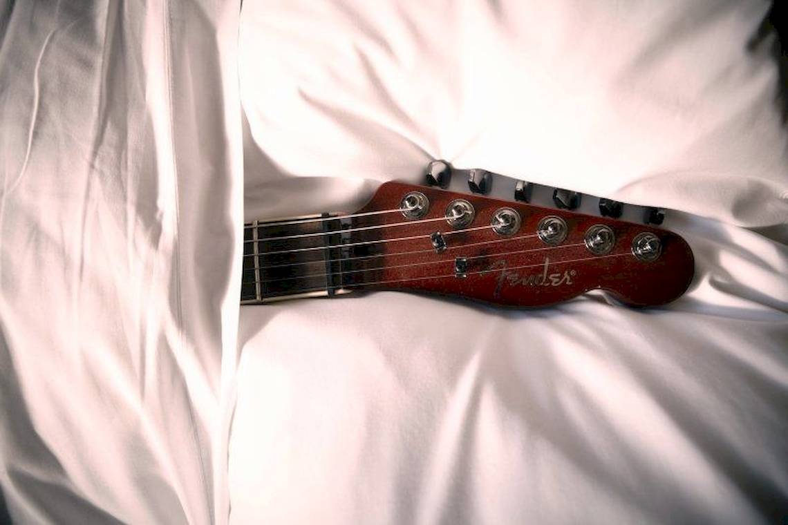 Der Hals einer roten Gitarre liegt auf einem weißen Laken.