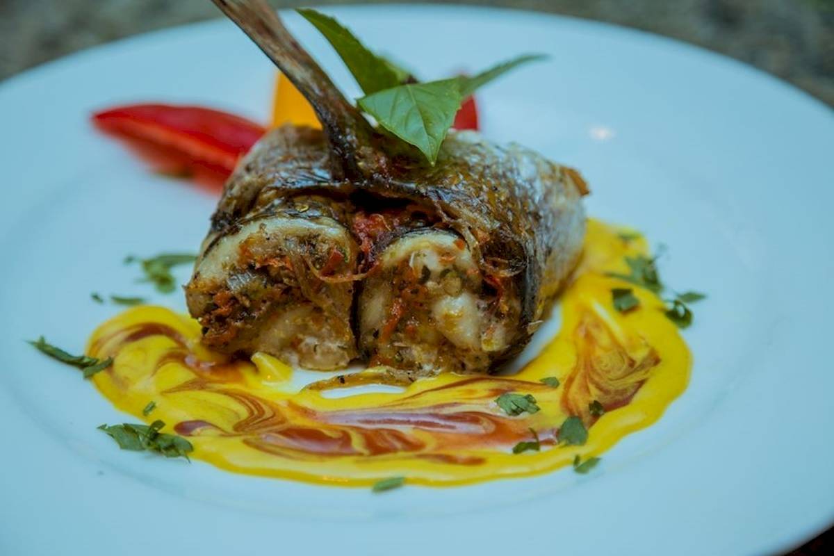 Gegrillter Fisch auf einem weißen Teller mit gelber Soße und grünen Blättern.