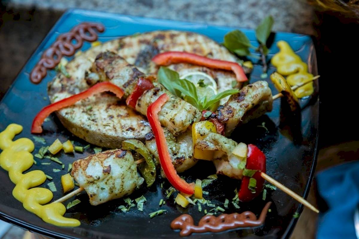 Gegrillter Fisch mit Gewürzen und Gemüse auf einem blauen Teller.