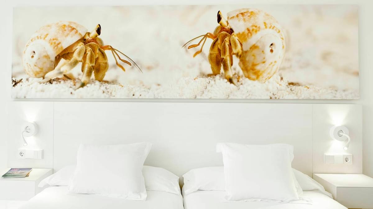 Hotelzimmer mit zwei Betten, weißen Kissen und Nachttischen, sowie einer Wand mit Meerestier-Bild.