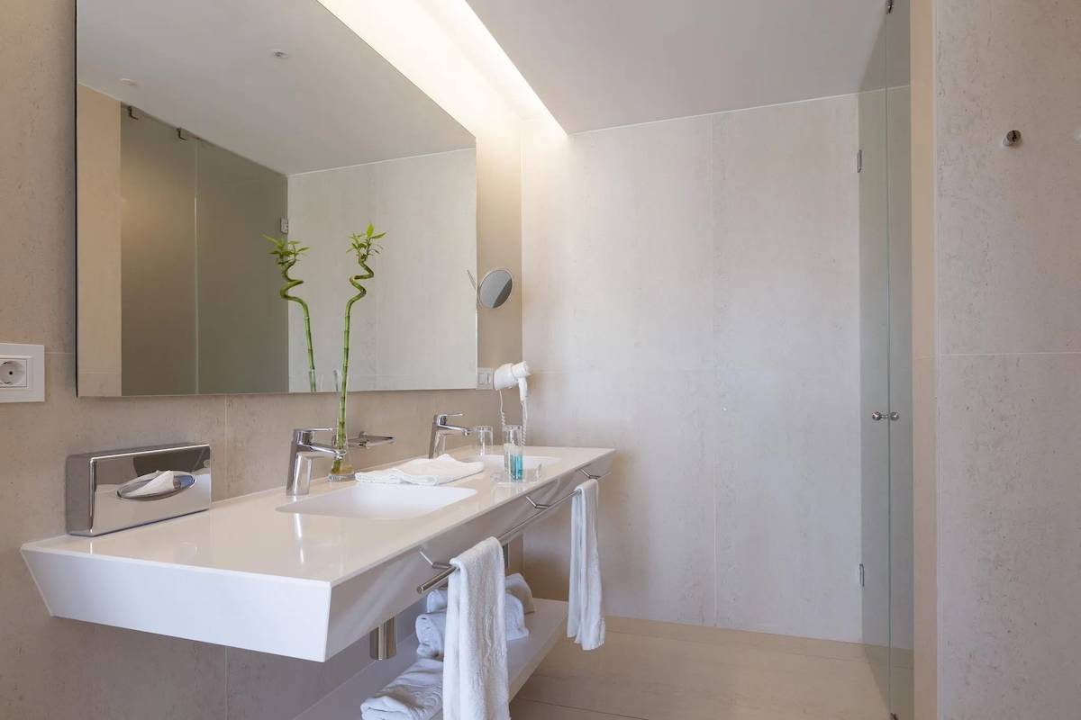 Badezimmer im Hipotels Gran Playa de Palma mit weißem Waschbecken, Spiegel und blauem Badezimmerzubehör.