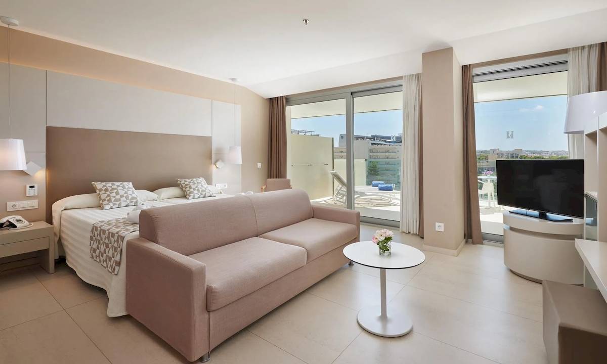 Modernes Hotelzimmer mit einem Sofa, einem Bett, einem Tisch und einem Fernseher auf einem Balkon.