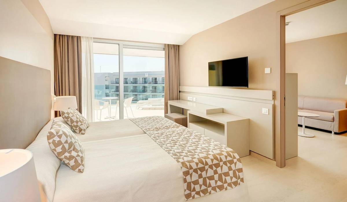 Innenansicht eines Hotelzimmers im Hipotels Gran Playa de Palma mit Doppelbett, Fernseher, Sofa und Terrassenblick.