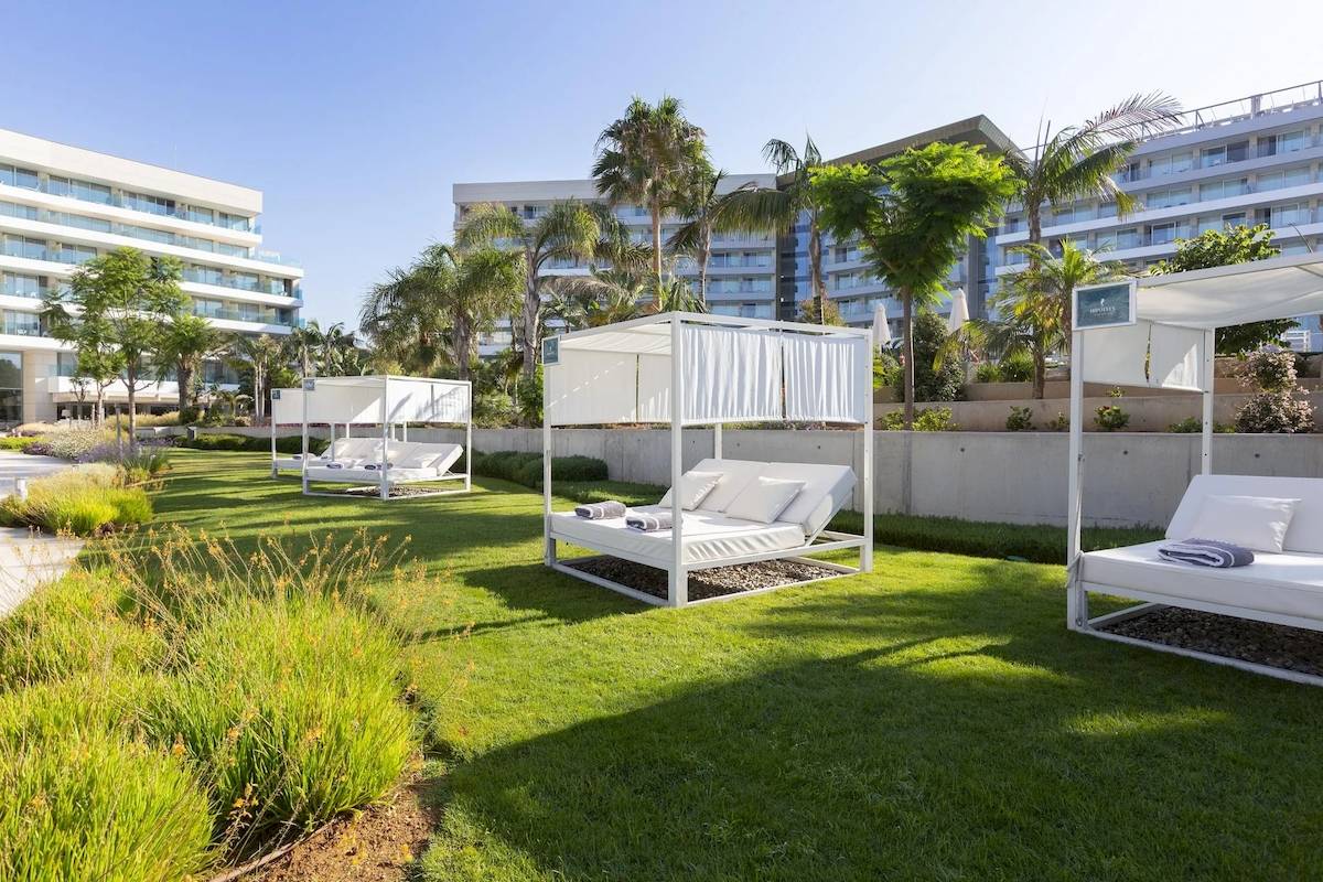 Aussenbereich des Hipotels Gran Playa de Palma mit weißen Sonnenbetten auf grünem Rasen