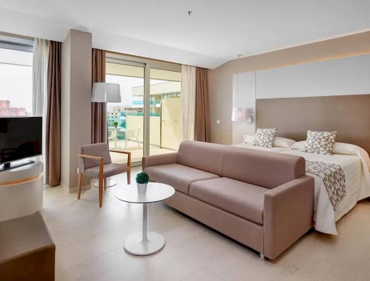 Innenansicht der Suite im Hotel Hipotels Gran Playa de Palma mit Bett, Sofa, Tisch und Fernseher.