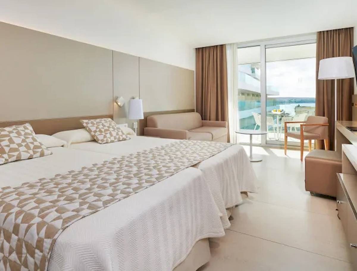 Schlafzimmer im Hipotels Gran Playa de Palma mit zwei Betten, einem Sofa und einem Tisch mit Blick auf das Meer.
