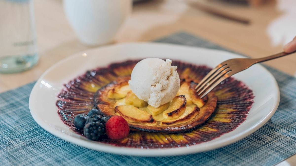 Ein Teller mit Apfelkuchen, Eis und Beeren auf einem blauen Tischtuch.