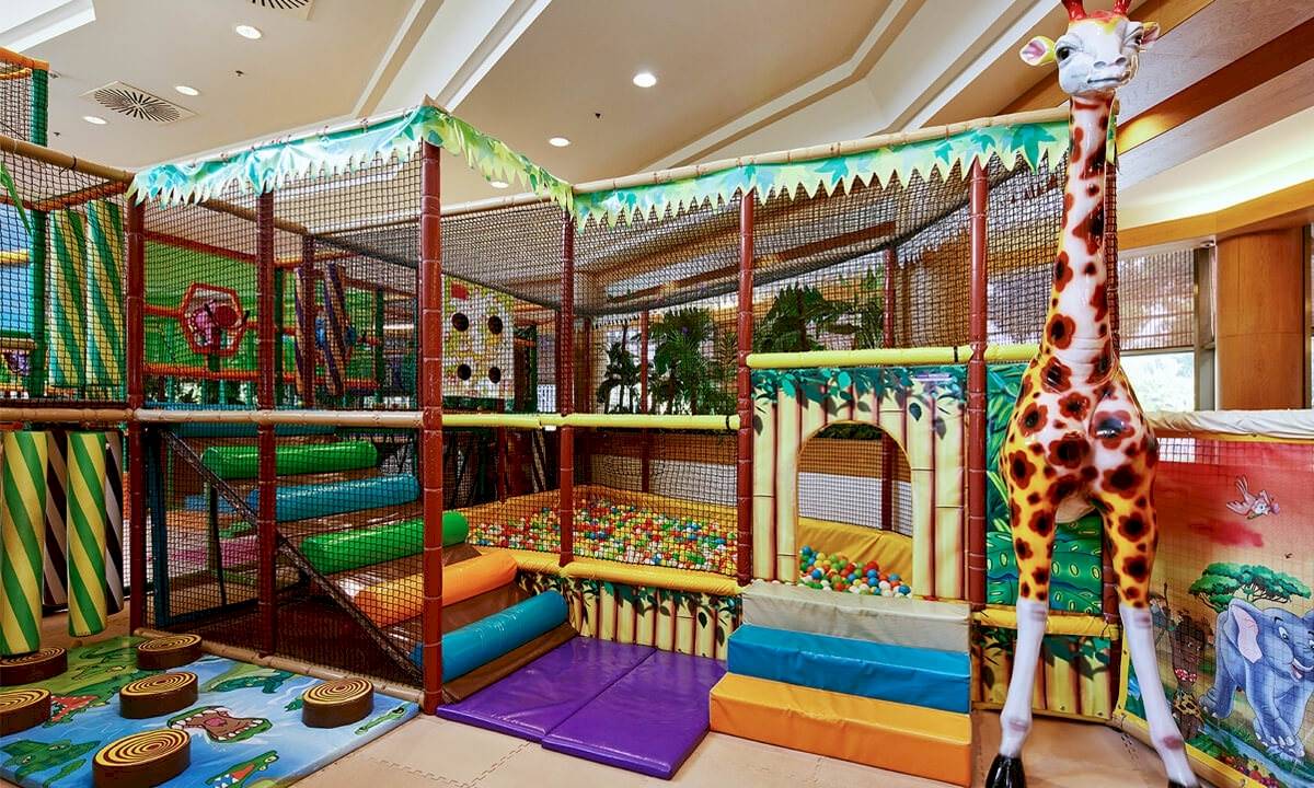 Kinderspielplatz im Gloria Golf Resort mit bunten Spielgeräten und einer großen Giraffenfigur.
