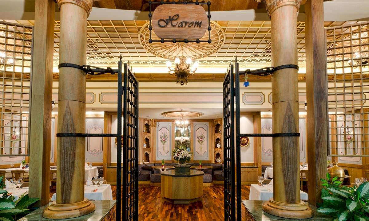 Innenansicht des Gloria Golf Resorts mit eleganten Säulen, einem offenen Eingang und einem runden Tisch mit Blumen in der Mitte.