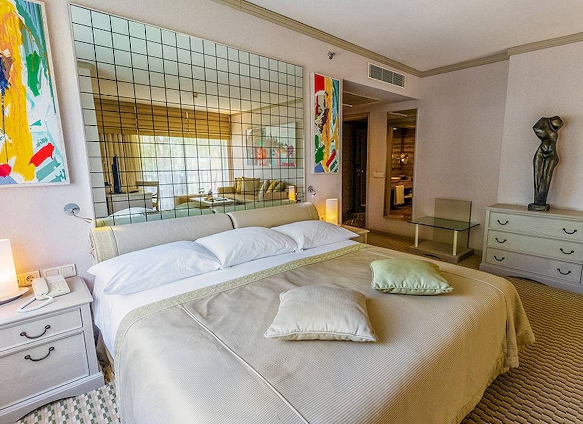 Schlafzimmer im Gloria Golf Resort Hotel mit einem großen Bett, zwei Kissen, einem Nachttisch und einem Spiegel