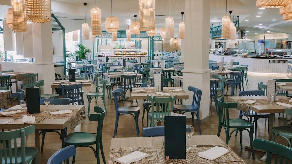 Innenansicht des Restaurants im Hotel Suites & Villas By Dunas mit blauen Stühlen und Holztischen.