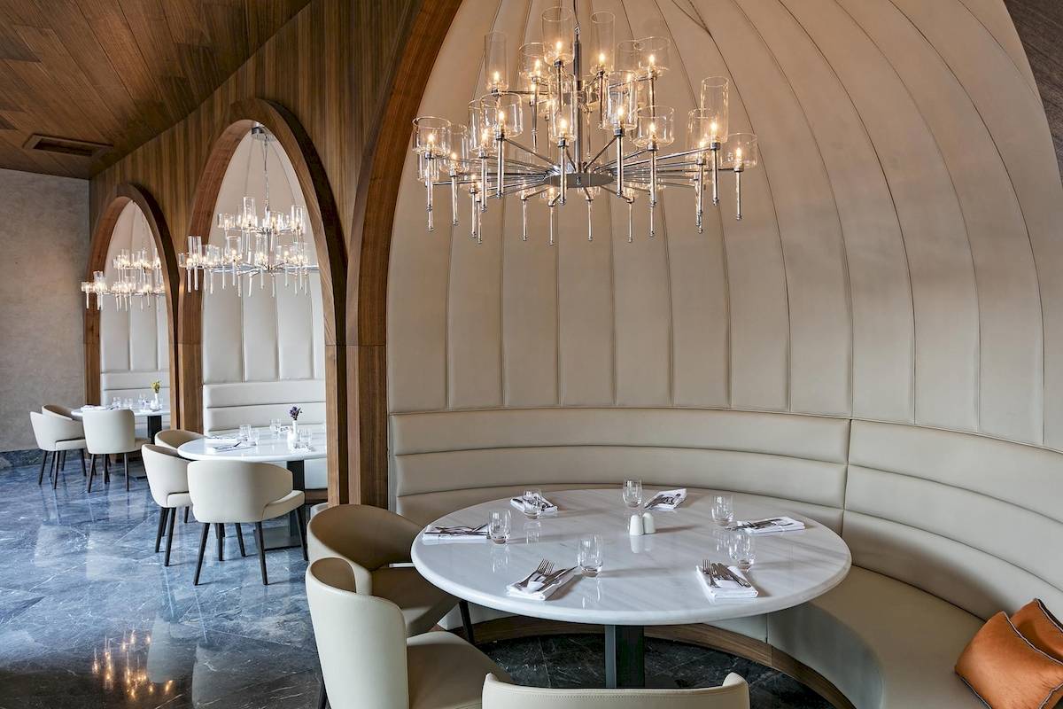 Innenansicht des Restaurants Titanic Luxury Collection Bodrum mit weißen Tischen, Stühlen und eleganten Leuchten.