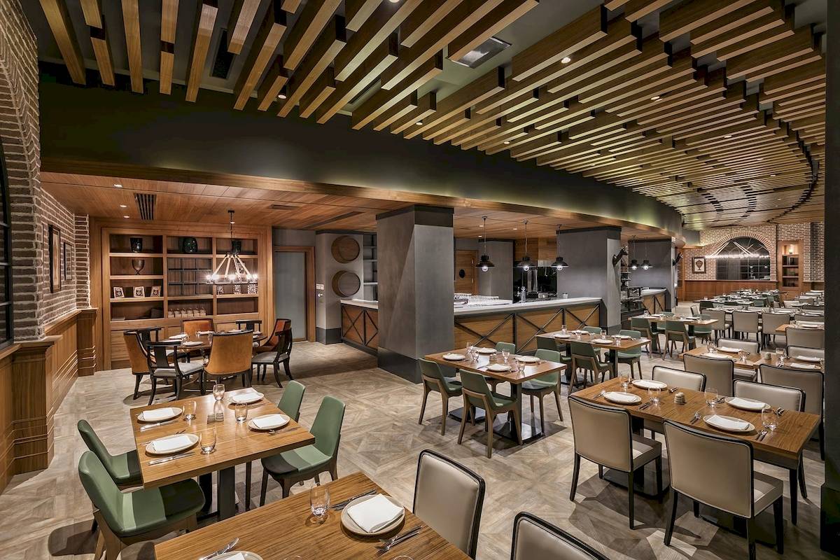 Innenansicht des Restaurants im Titanic Luxury Collection Bodrum Hotel mit Holztischen, Stühlen und einem offenen Bereich mit einer Bar.
