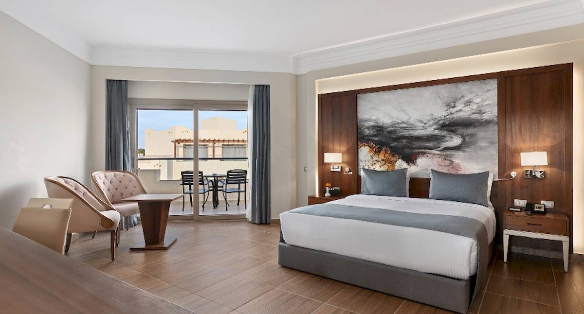 Innenansicht eines Zimmers im Xanadu Makadi Bay Hotel mit Bett, Sesseln und Terrassentür.