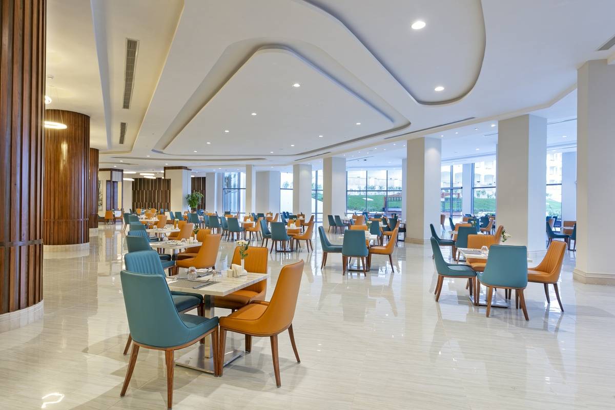 Innenansicht des Restaurants im Xanadu Makadi Bay Hotel mit blauen und orangefarbenen Stühlen und Tischen.