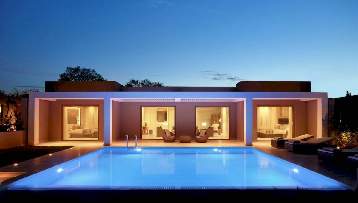 Nachtansicht der Ikos Dassia Villa mit beleuchtetem Pool und offenen Fenstern.
