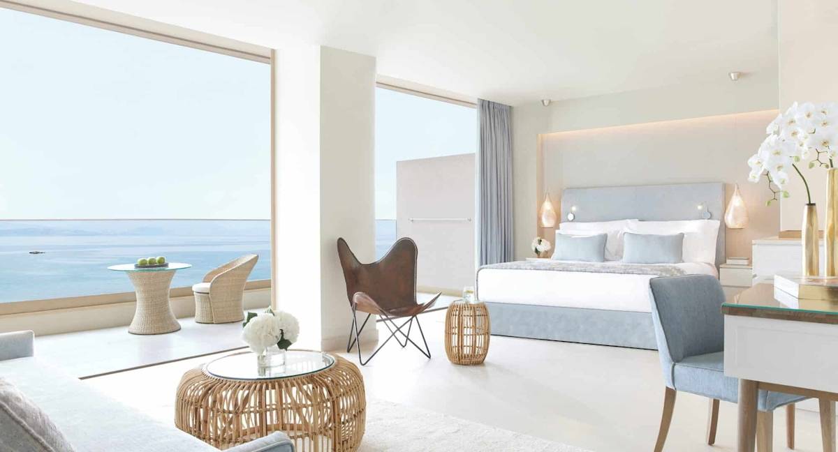 Modernes Hotelzimmer mit Meerblick im Ikos Dassia, mit großen Fenstern, einem Bett, und einem Ausblick auf den Ozean.