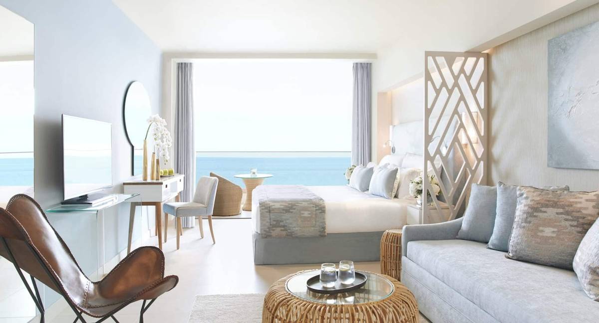Zimmer im Ikos Dassia Hotel mit Meerblick, Bett, Schreibtisch, Fernseher und Möbeln.