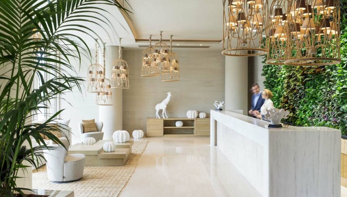 Empfangsbereich des Ikos Dassia Hotels mit modernem Design, weißen Möbeln, Pflanzen und einer Statue.
