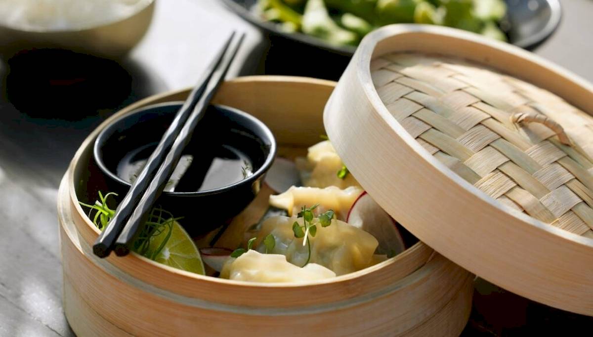 Dampfende asiatische Dumplings in einem Korb mit Soße und Chopsticks